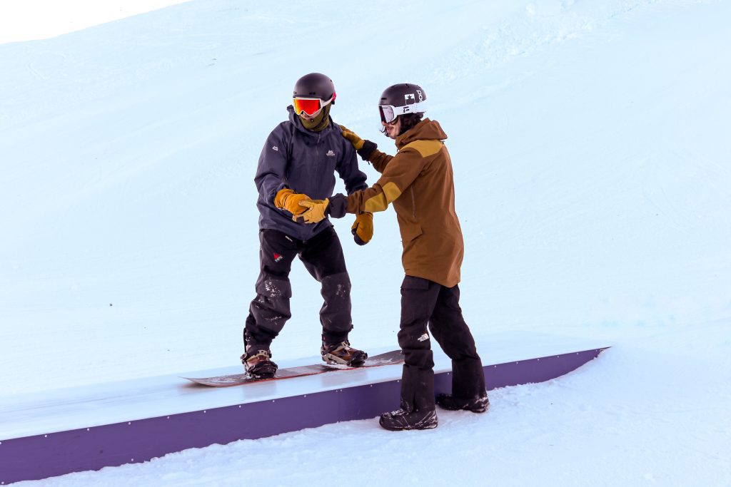 Snowboard instructor helping a student balance on a box in the snowpark in Engelberg