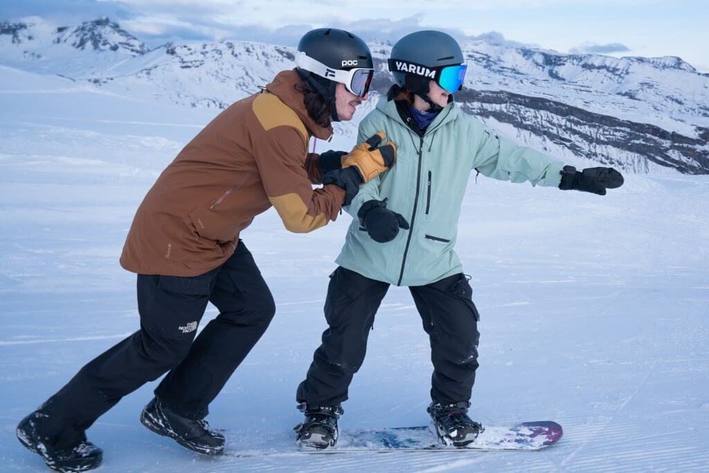 Snowboard instructor guiding a beginner through their first turns on a groomed slope in Engelberg