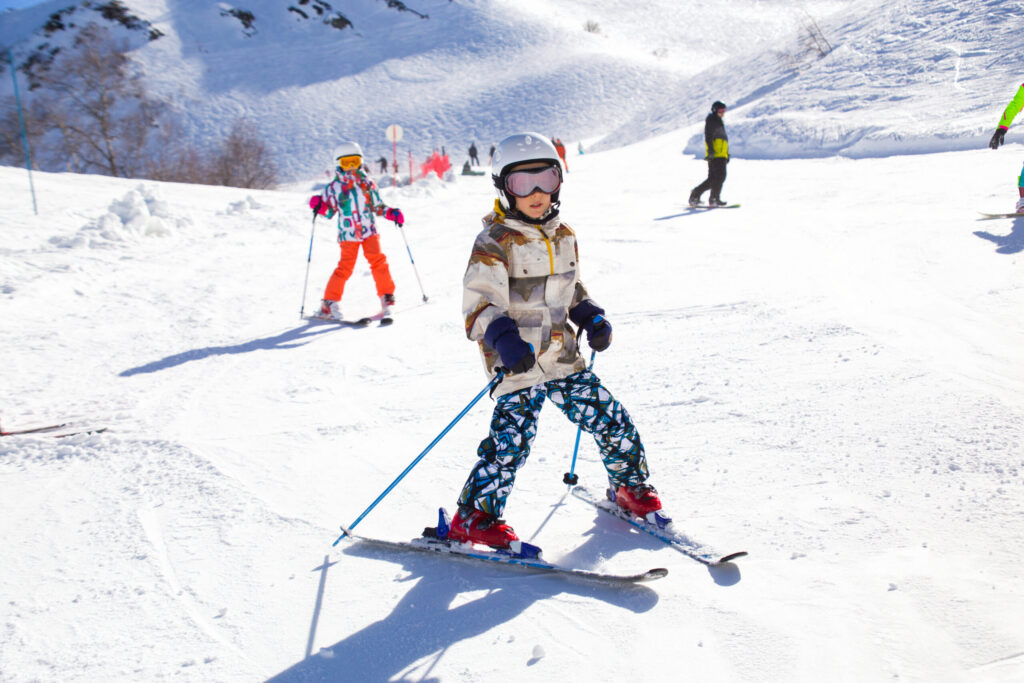 A child in a helmet practising a snowplough on a sunny beginner slope