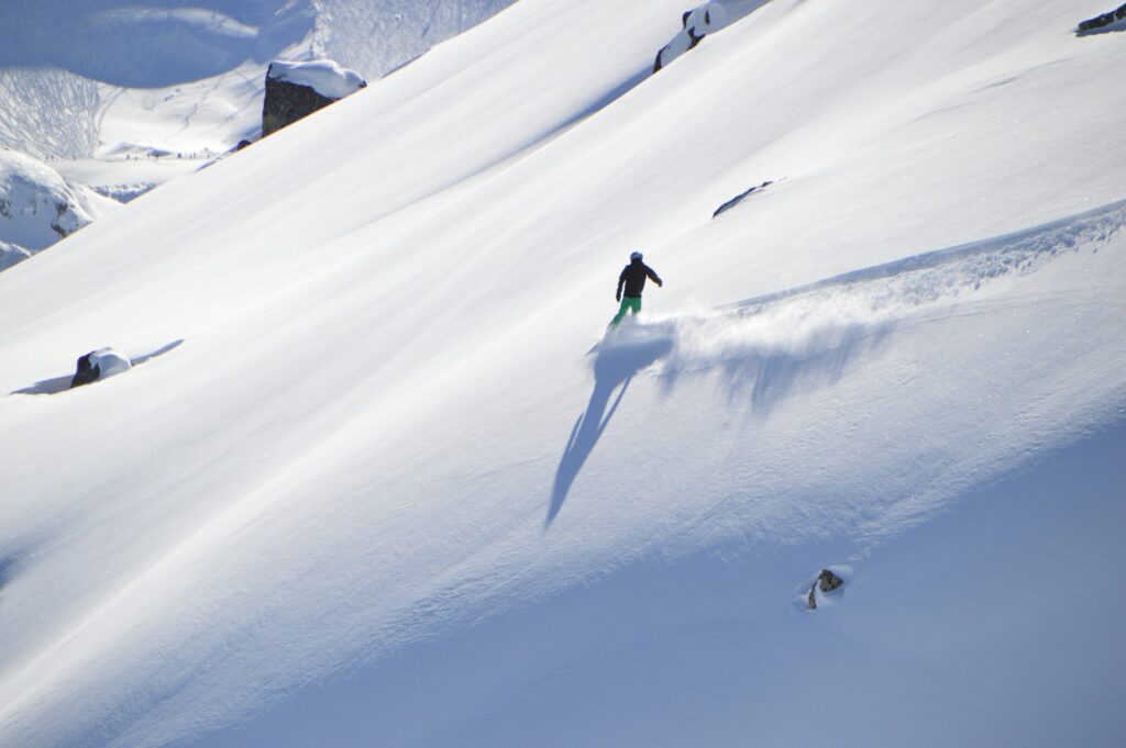 A snowboarder turning in fresh snow on a sunny slope off the piste