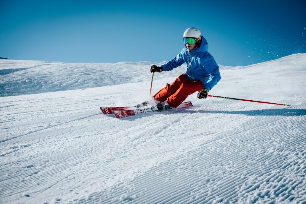 A skier in a blue jacket and red trousers carving a turn on a freshly groomed piste