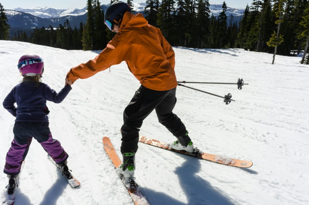 A ski instructor leads a young child by the hand on a gentle slope