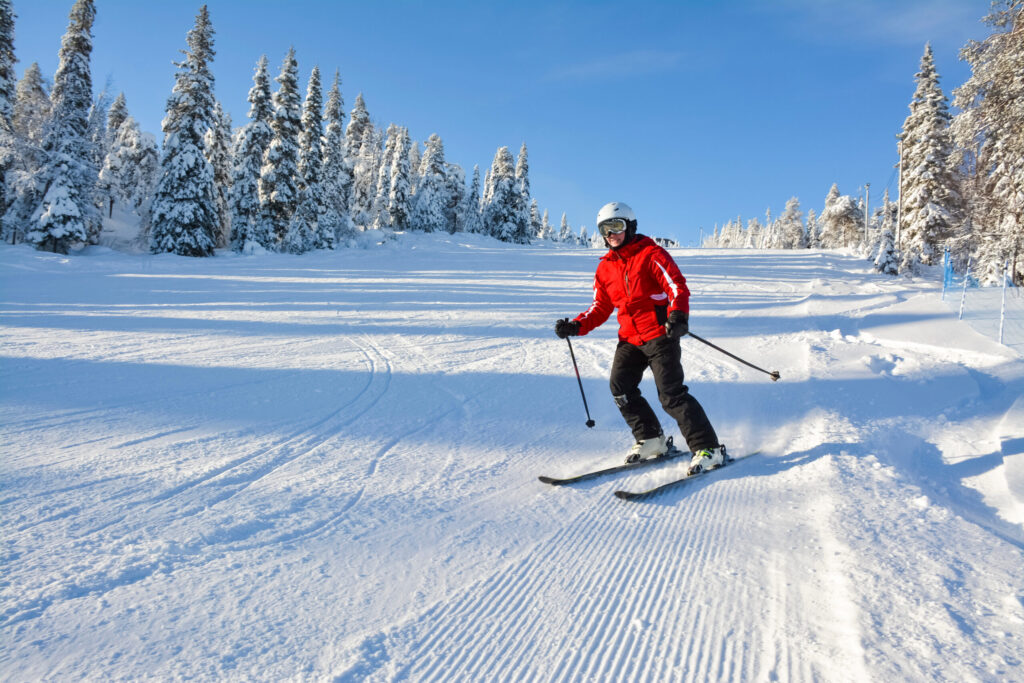 A skier in a red jacket making a controlled turn on a wide groomed slope