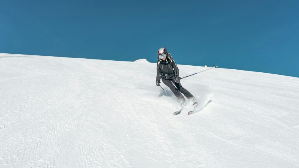 A skier turning on a wide, open piste under a blue sky