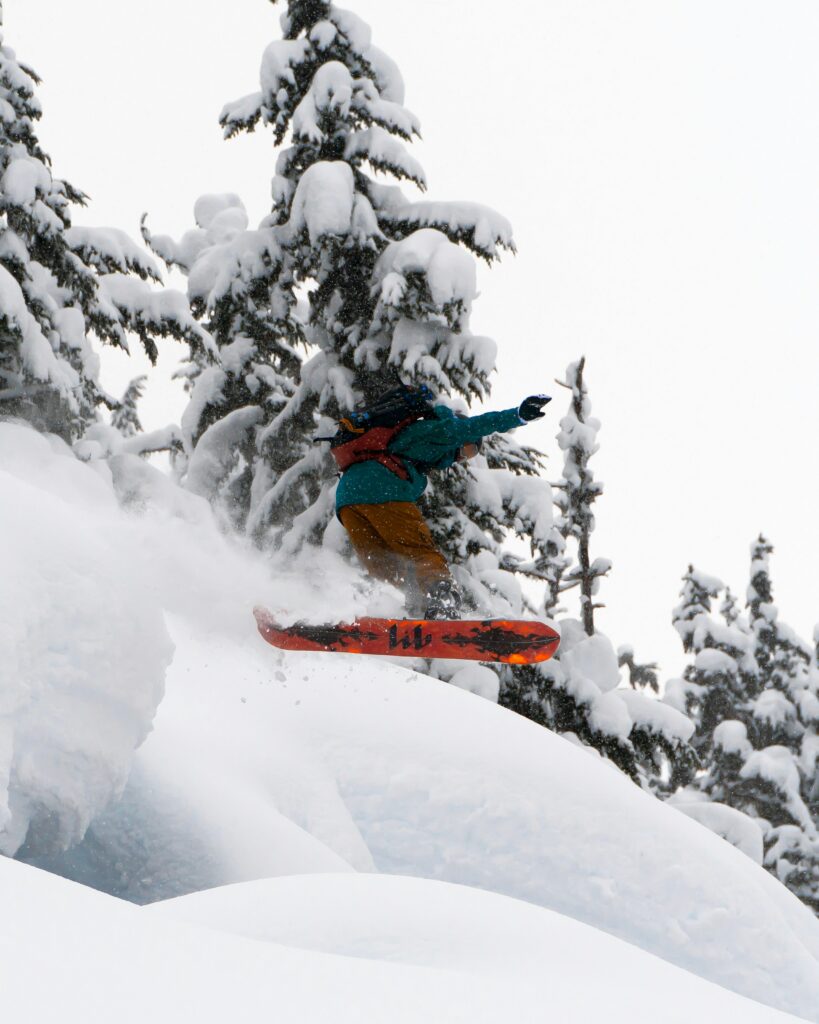 A snowboarder flying through fresh powder between snowy trees