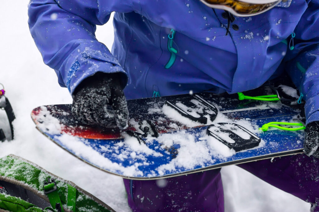 Gloved hands fitting climbing skins to the two halves of a splitboard